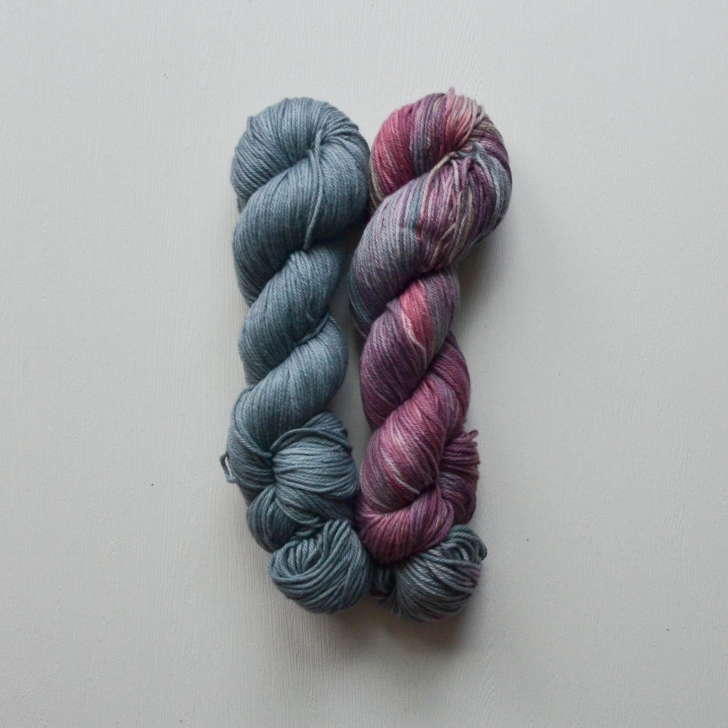 Two skeins of yarn, one blue and one pink, on a light gray background