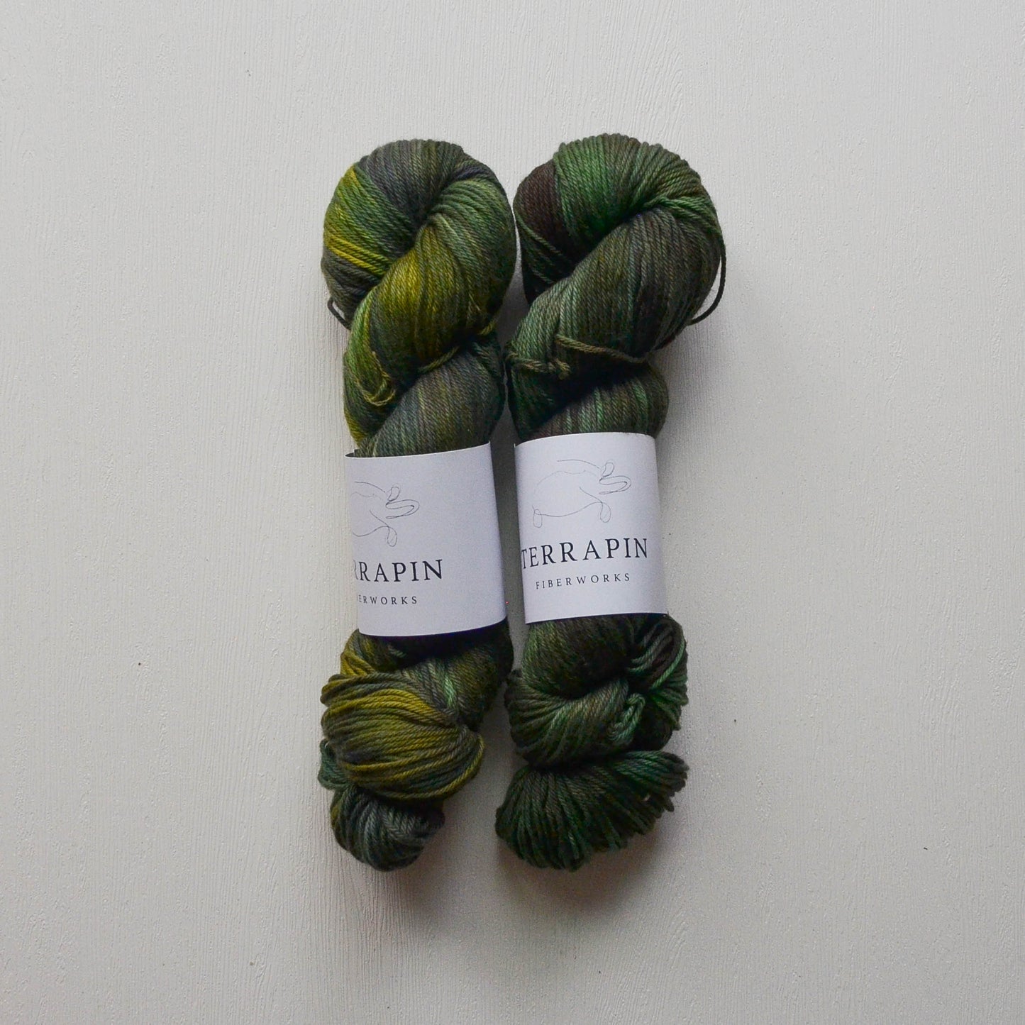 Two skeins of green yarn with labels on a white background