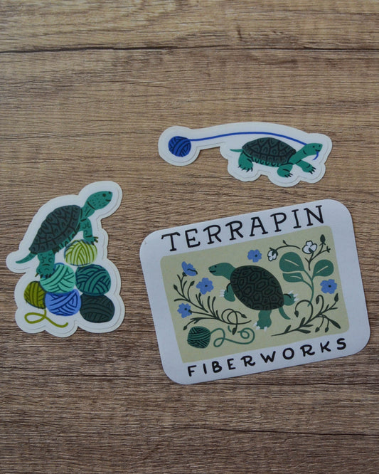 Three stickers featuring turtles and yarn on a wooden surface, with 'Terrapin Fiberworks' branding.